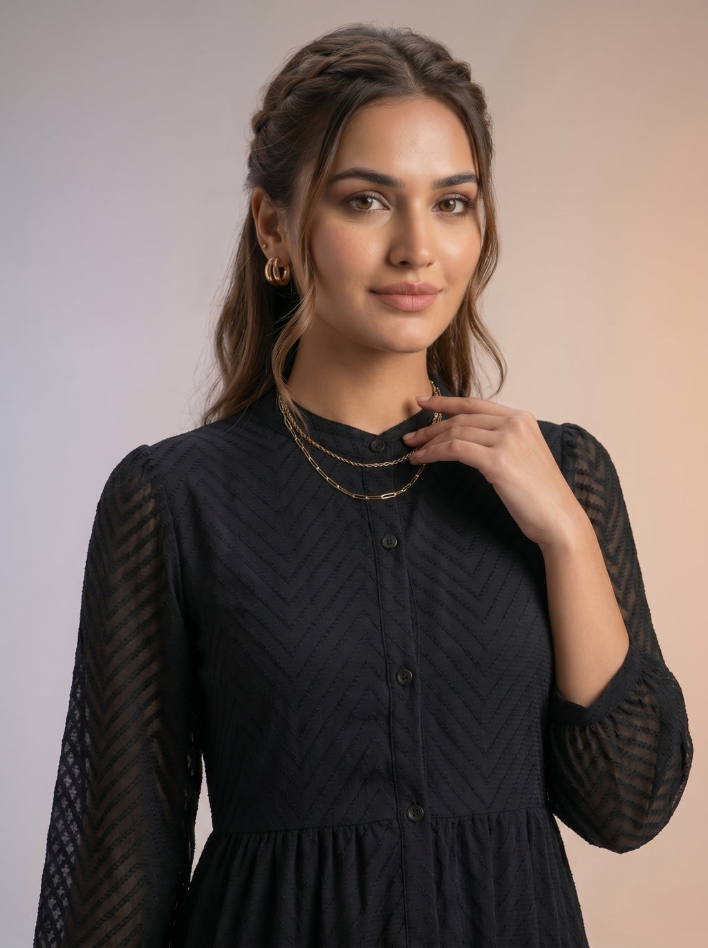 Woman wearing a black dress with sheer sleeves against a plain background