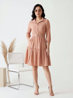 Woman wearing a pink dress standing in a minimalistic room with a chair and decorative elements.
