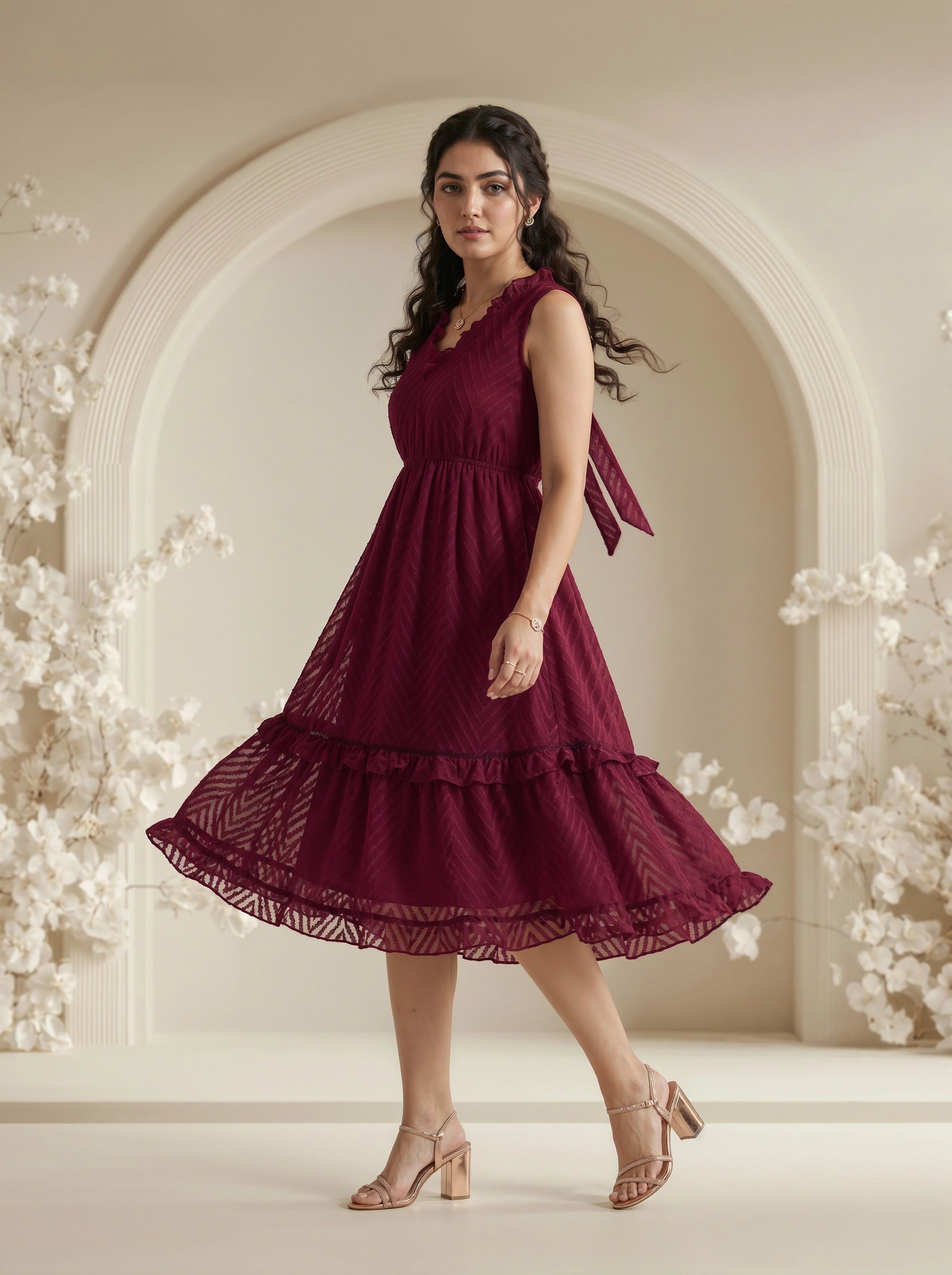 Woman wearing a burgundy dress standing in a decorated room with floral elements.