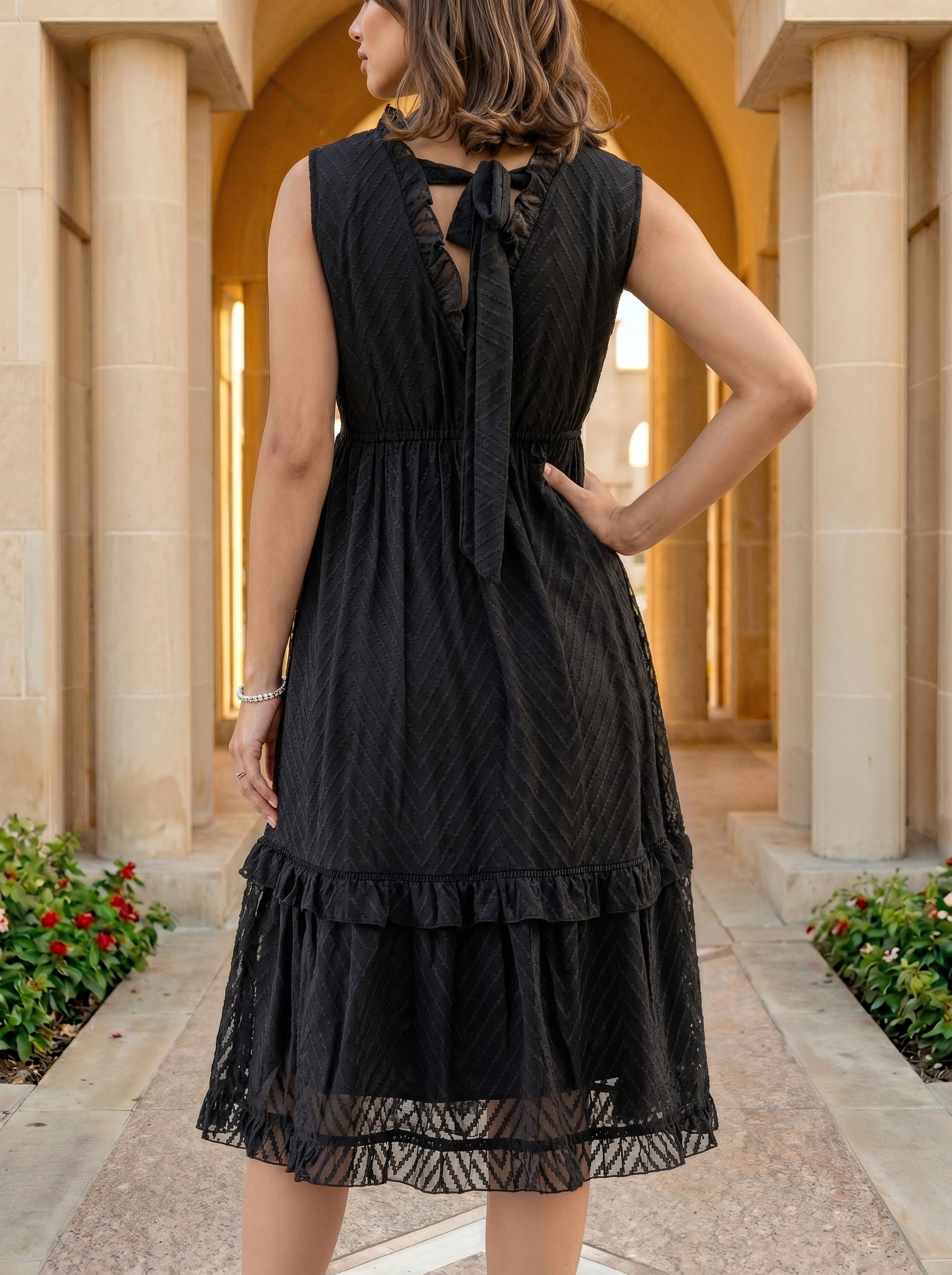 Woman wearing a black dress with a lace detail in an outdoor setting with columns and plants.