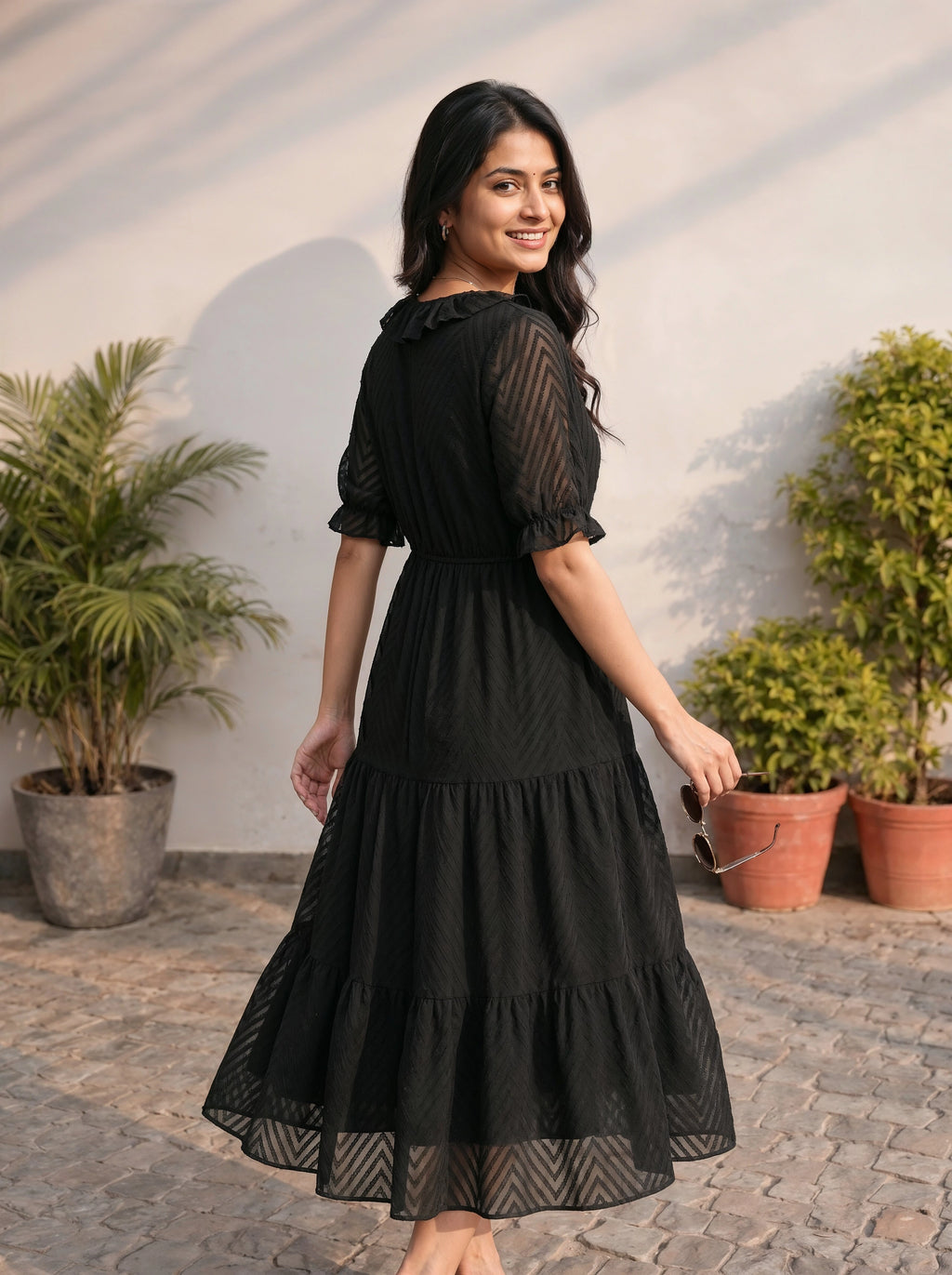 Woman wearing a black dress standing outdoors with plants in the background