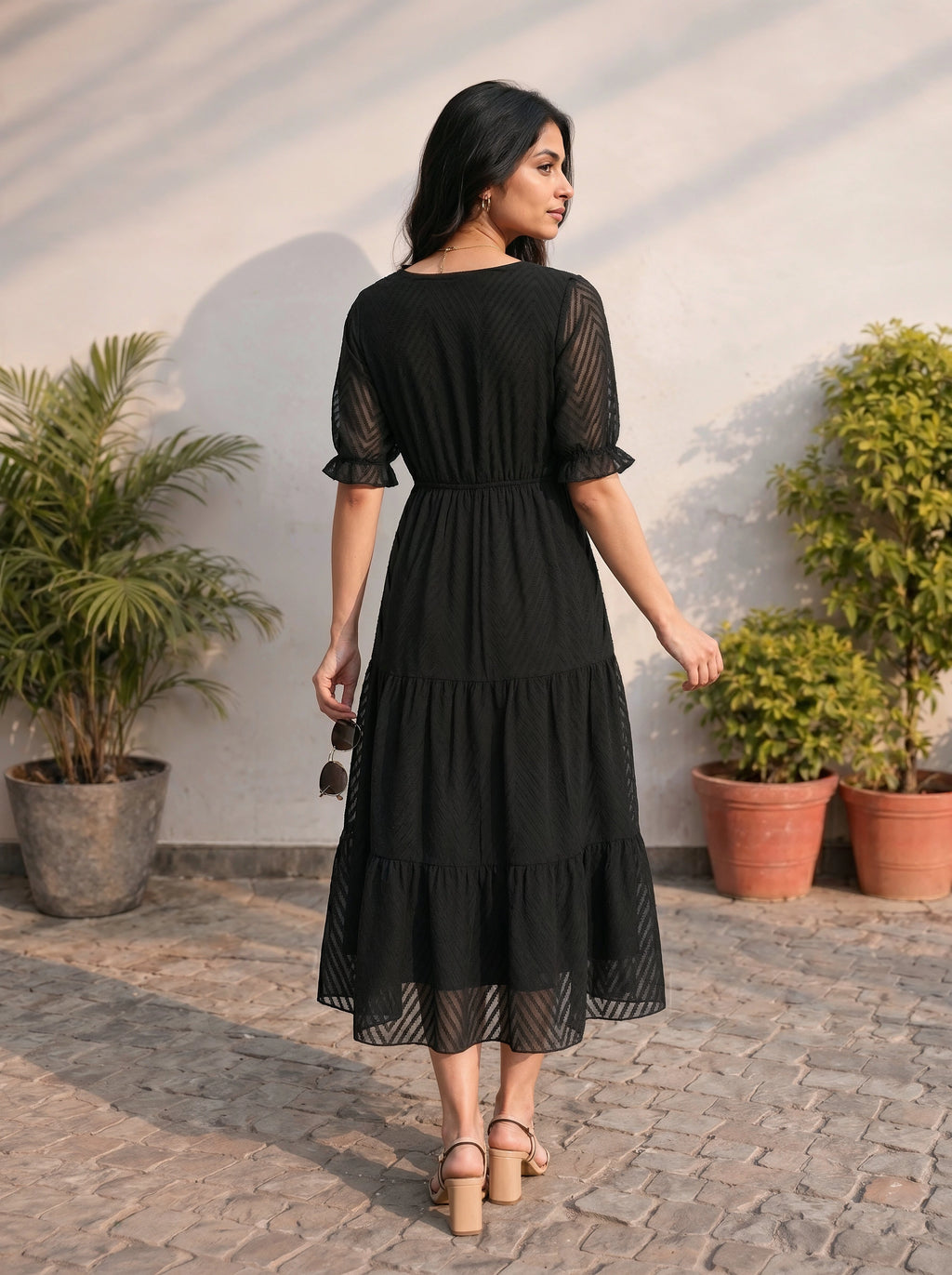 Woman in a black dress standing outdoors with plants in the background