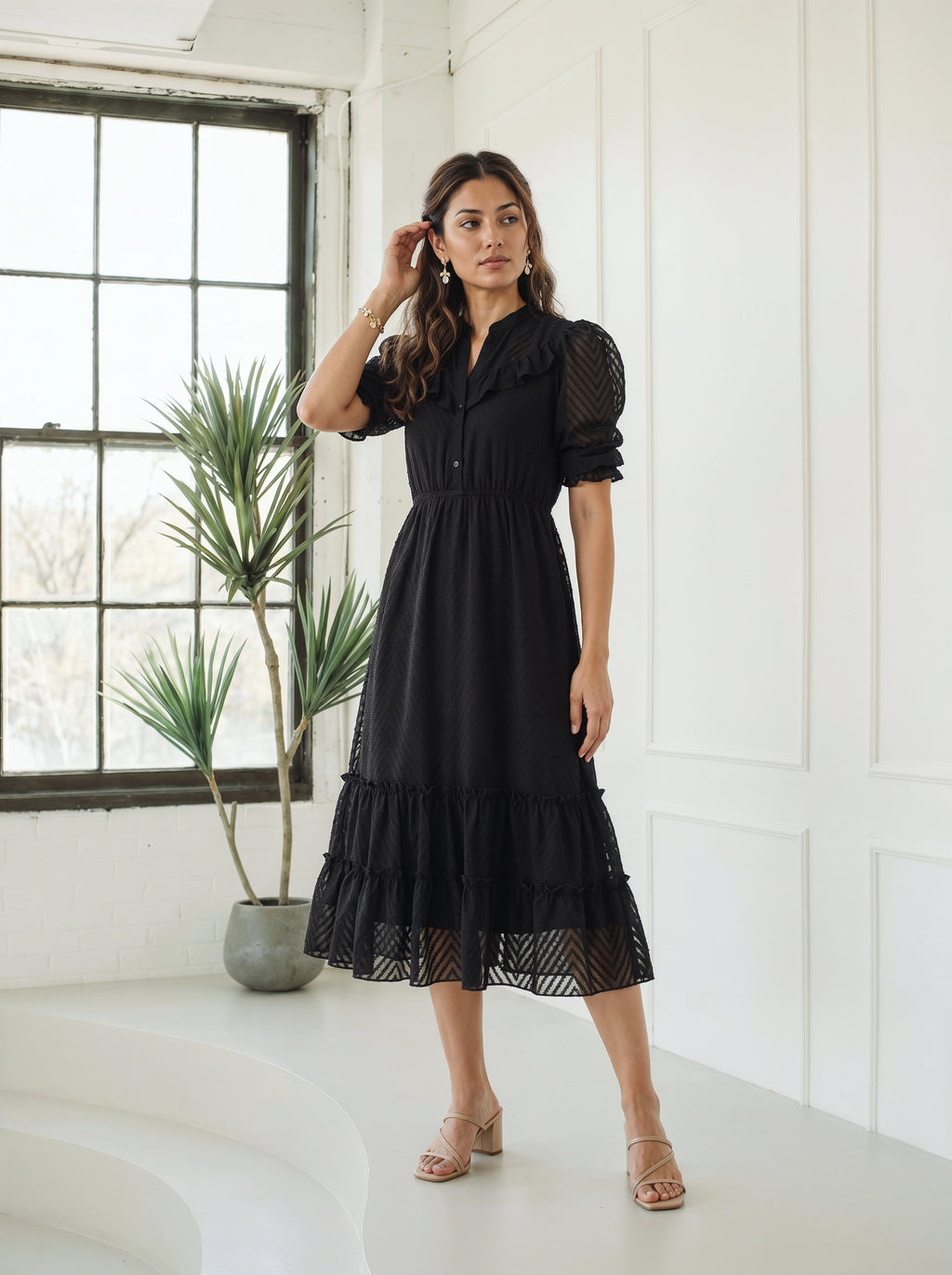 Woman standing indoors wearing a textured black midi dress