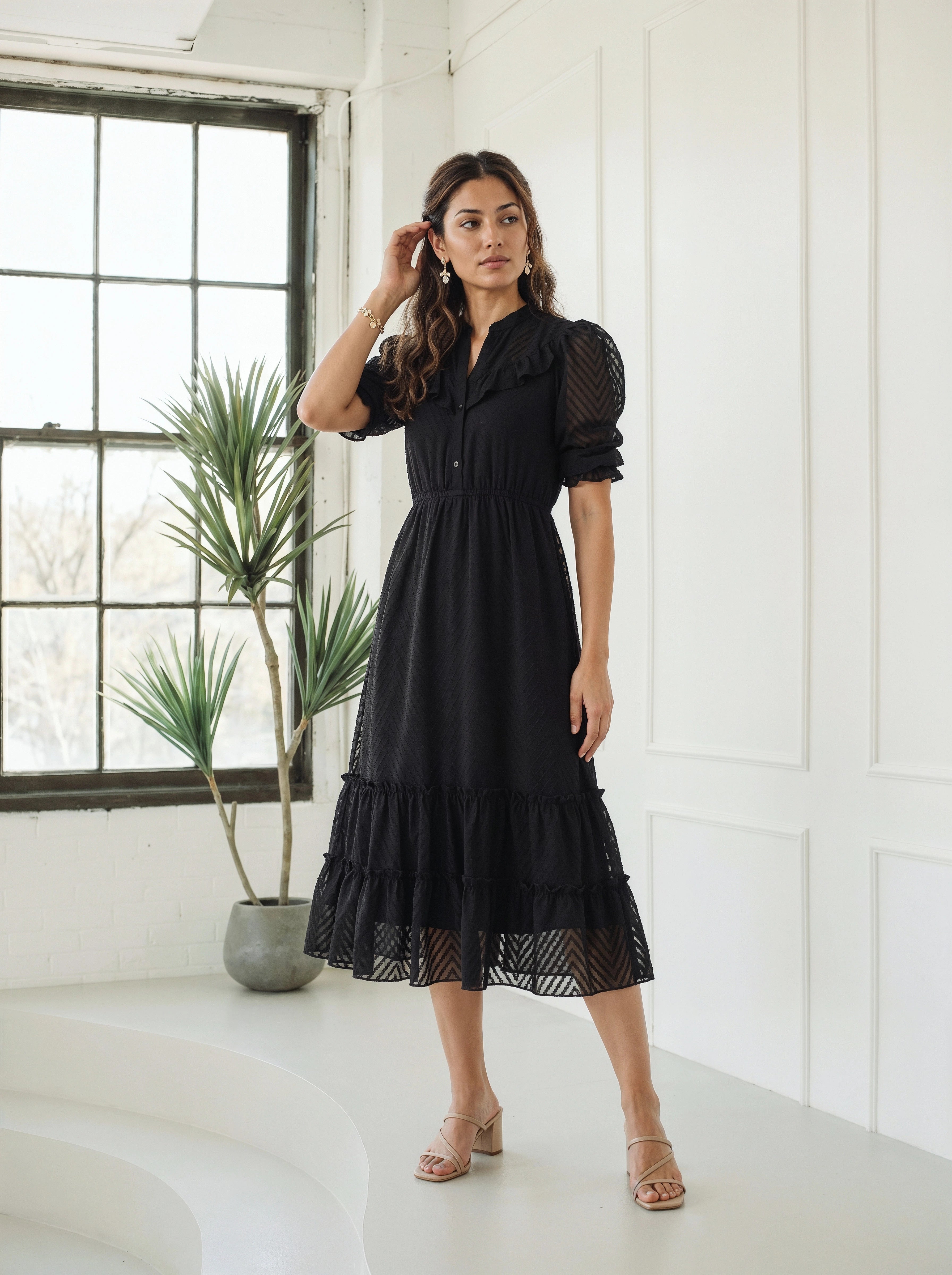 Woman standing indoors wearing a textured black midi dress