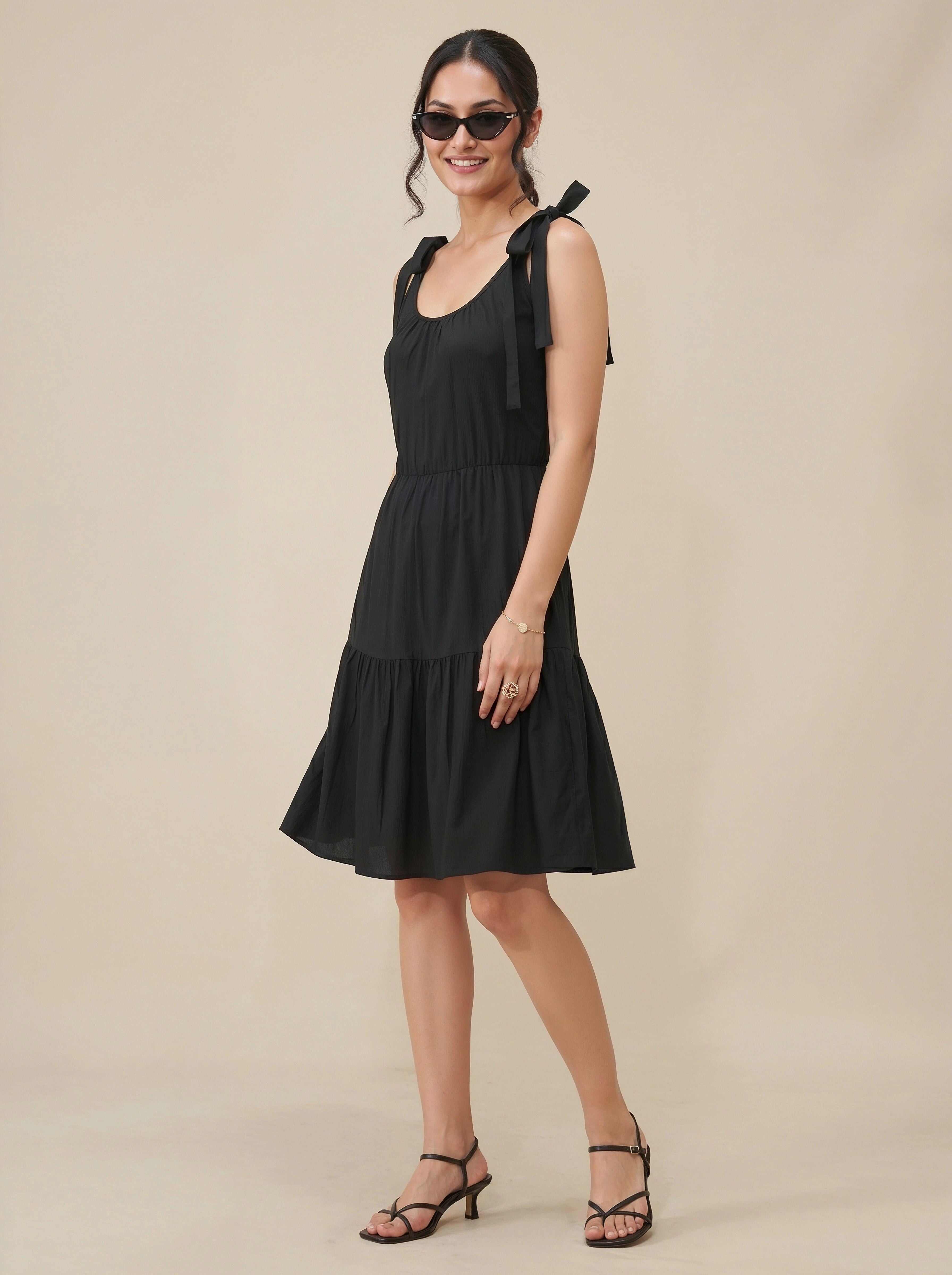 Woman wearing a black dress with bow straps against a beige background