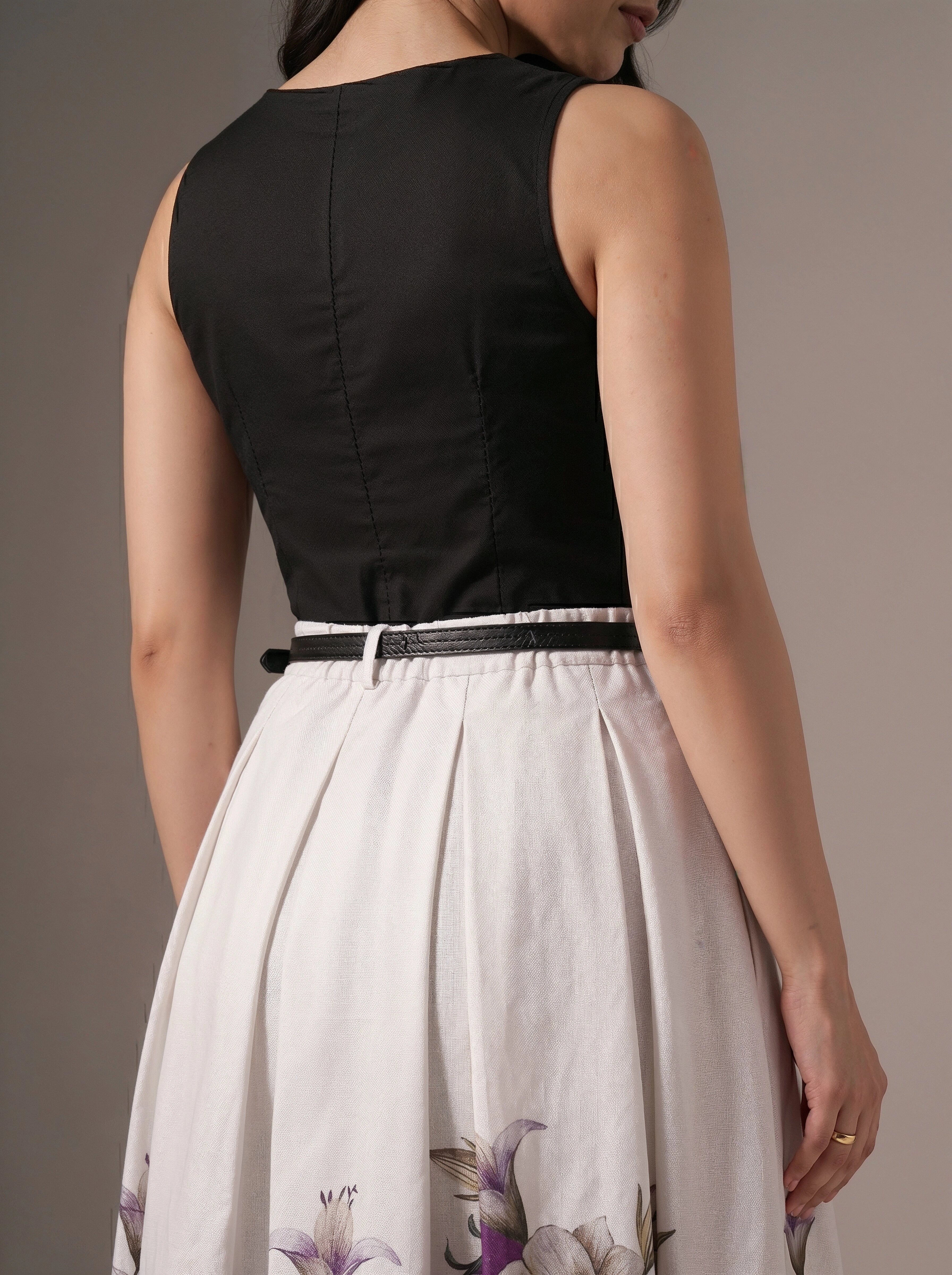 Person wearing a black top and white floral skirt against a neutral background