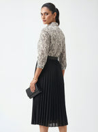 Woman wearing a patterned blouse and black pleated skirt holding a clutch on a white background