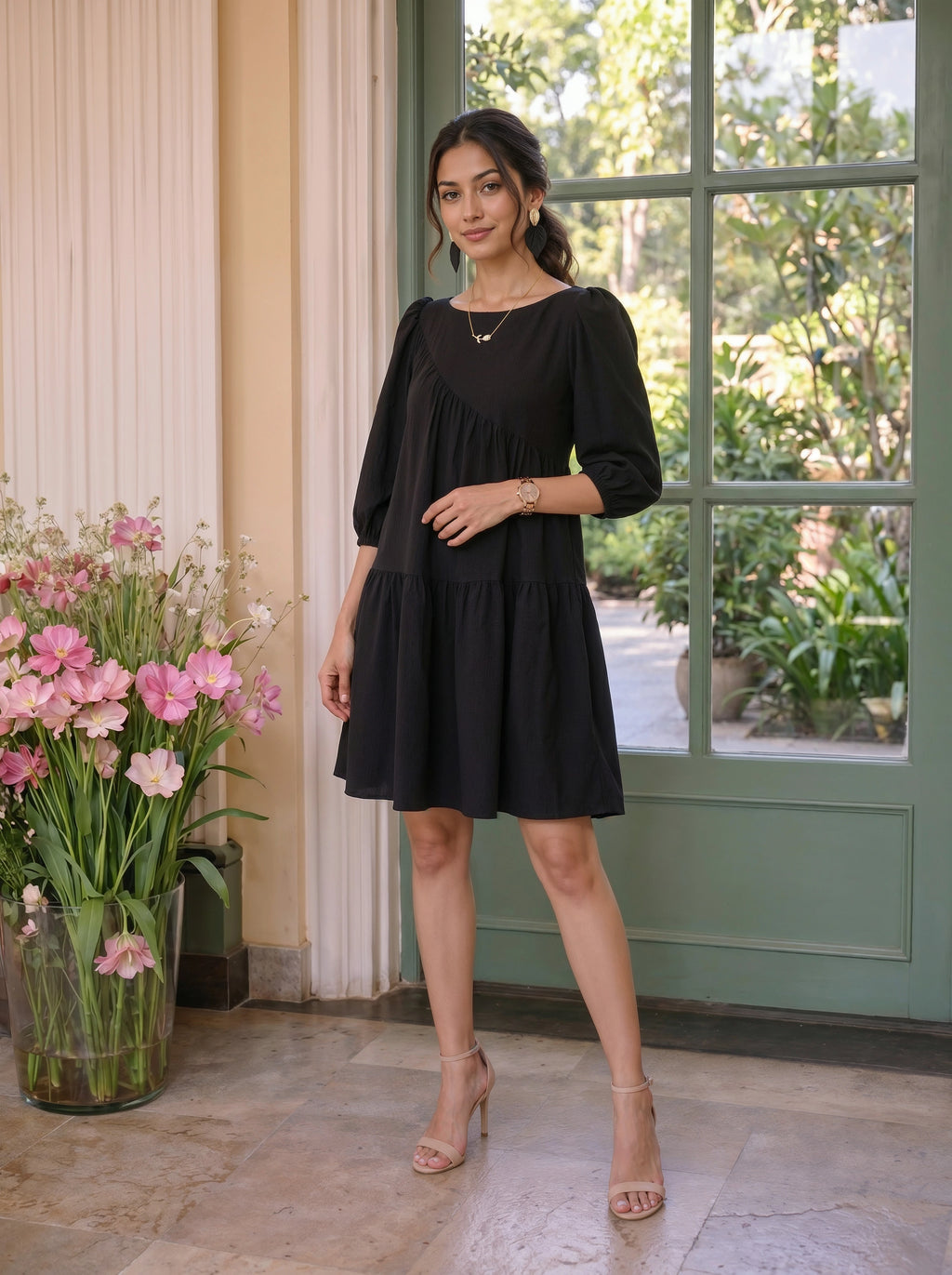 Woman in a black dress standing in a room with flowers and a door in the background