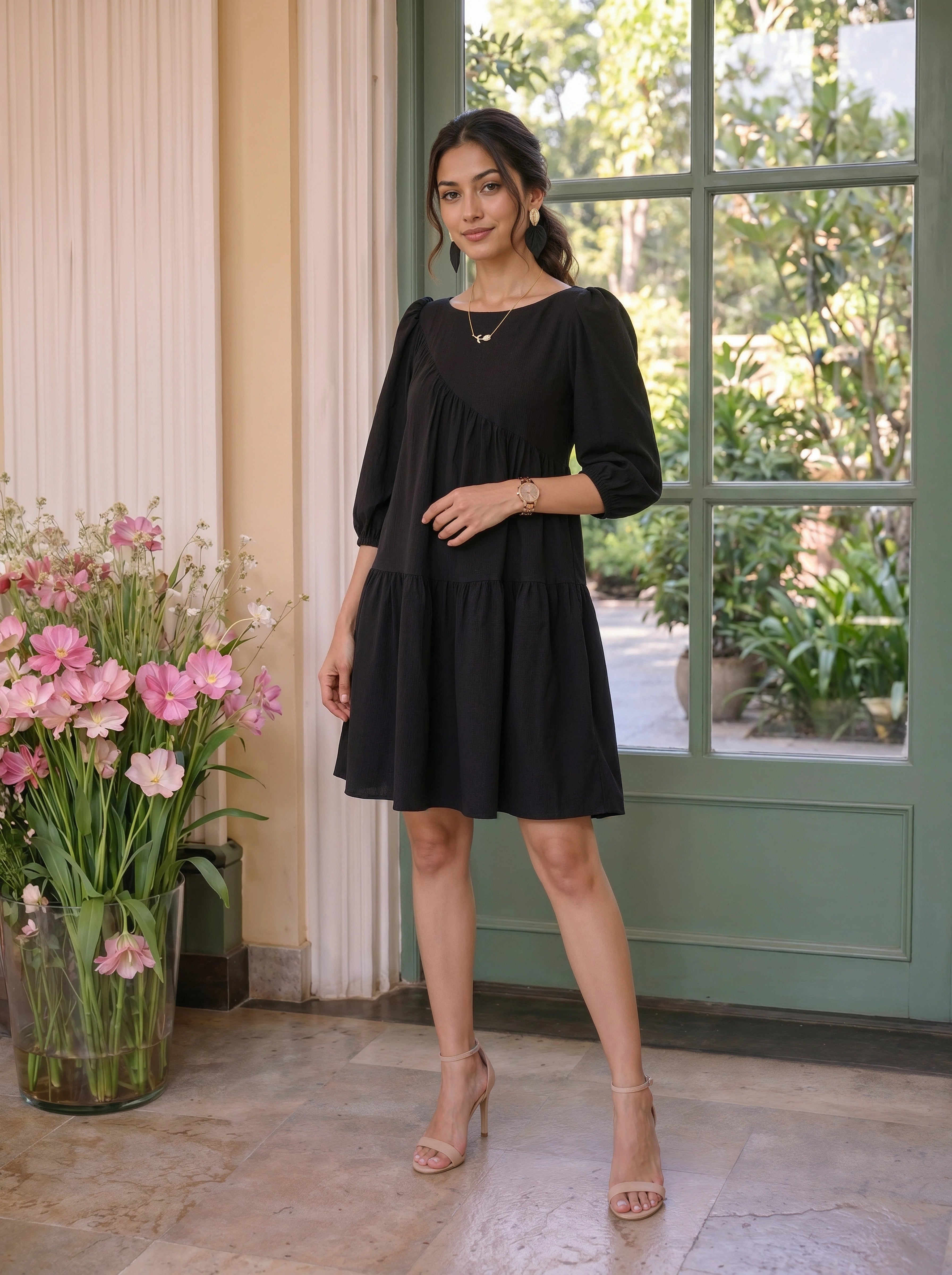 Woman in a black dress standing in a room with flowers and a door in the background