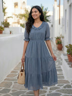 Woman in a blue dress standing on a stone path with plants and buildings in the background