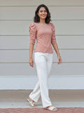 Woman wearing a peach top and white pants standing on a porch.