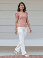 Woman wearing a peach top and white pants standing on a porch.