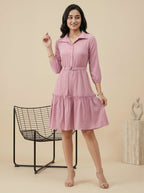 Woman wearing a pink dress standing in a minimalistic room with a chair and sculpture.
