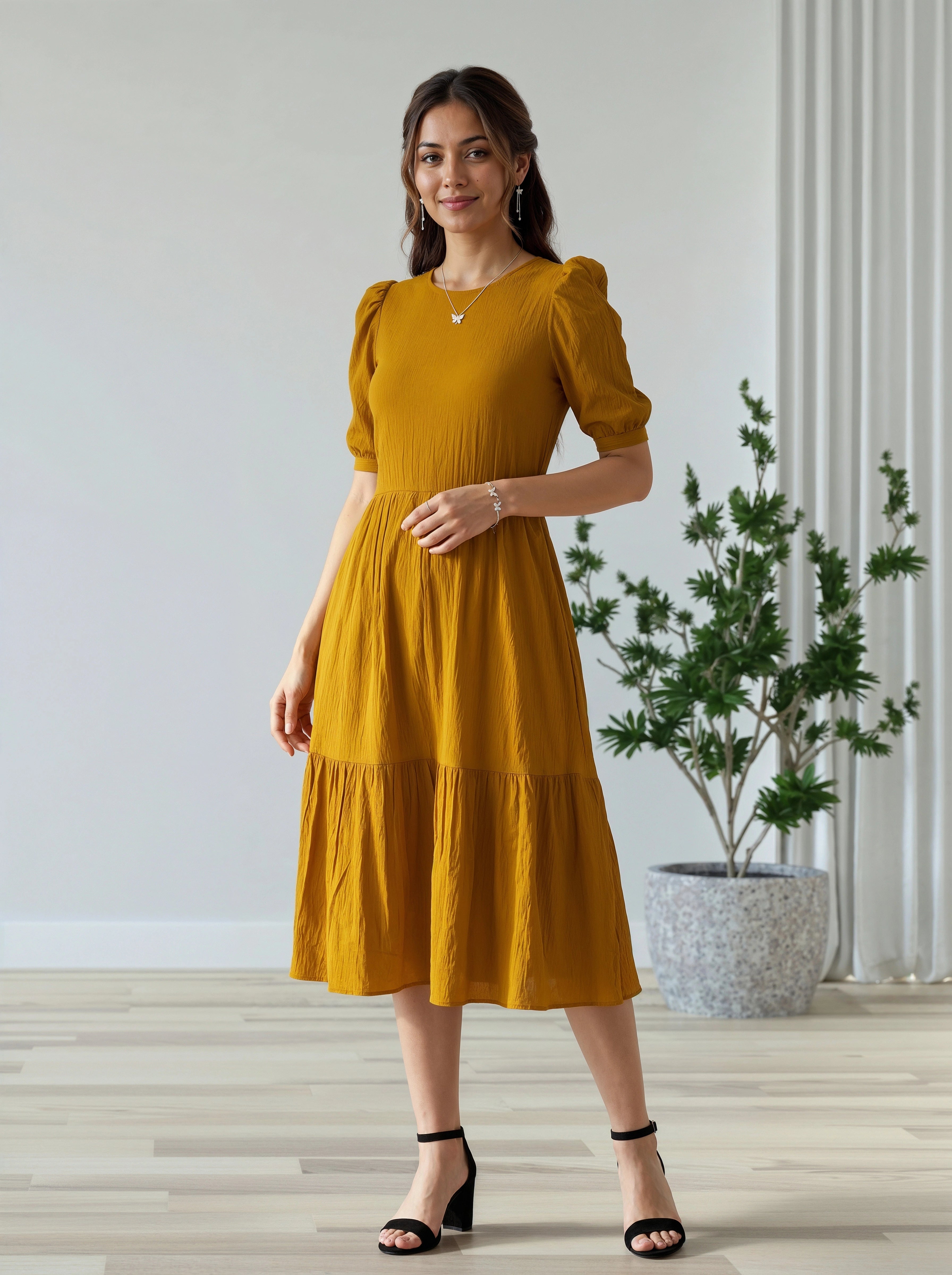 Woman wearing a mustard yellow dress standing indoors with a plant in the background