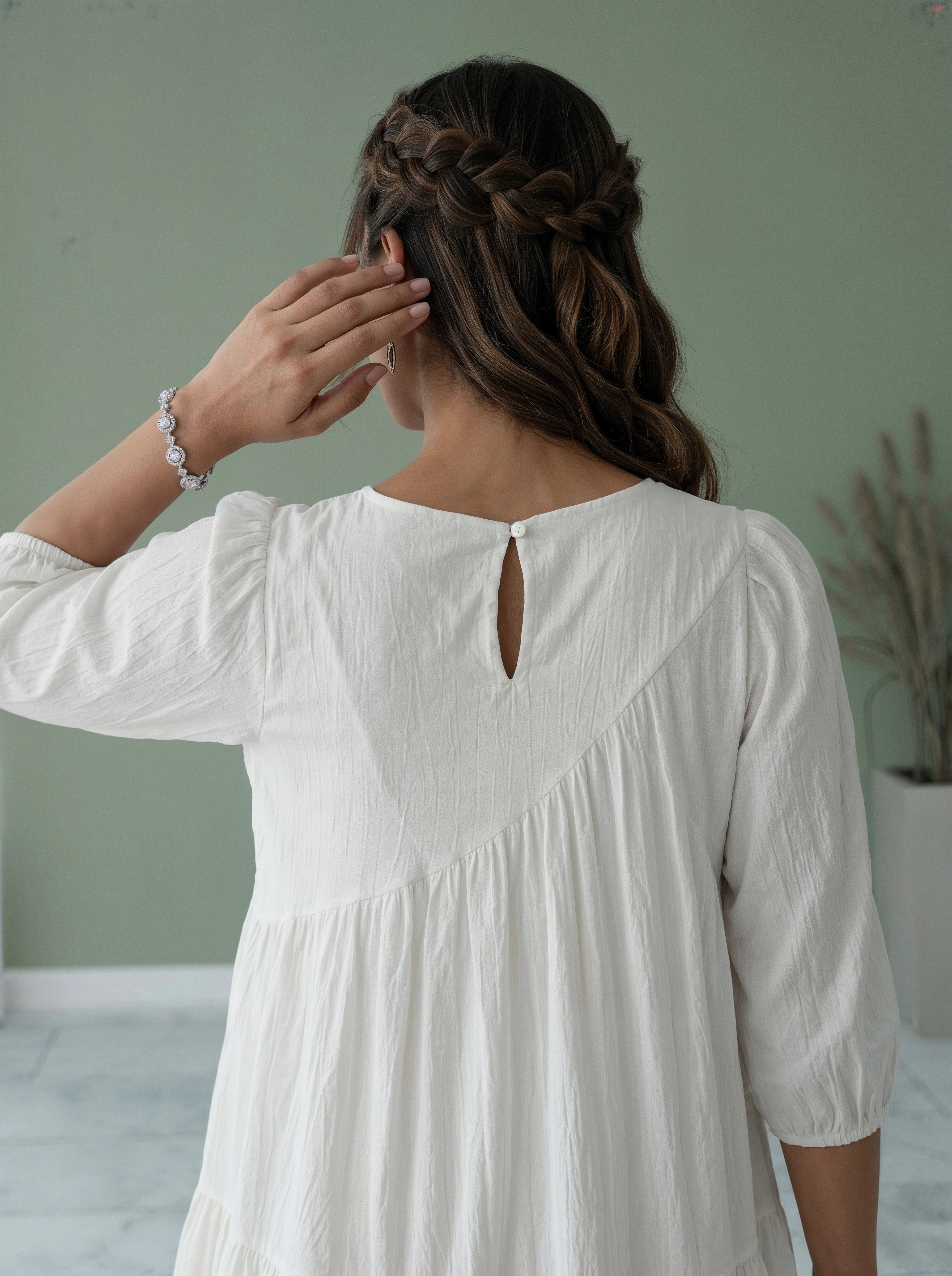 Woman in a white dress with braided hair against a plain background