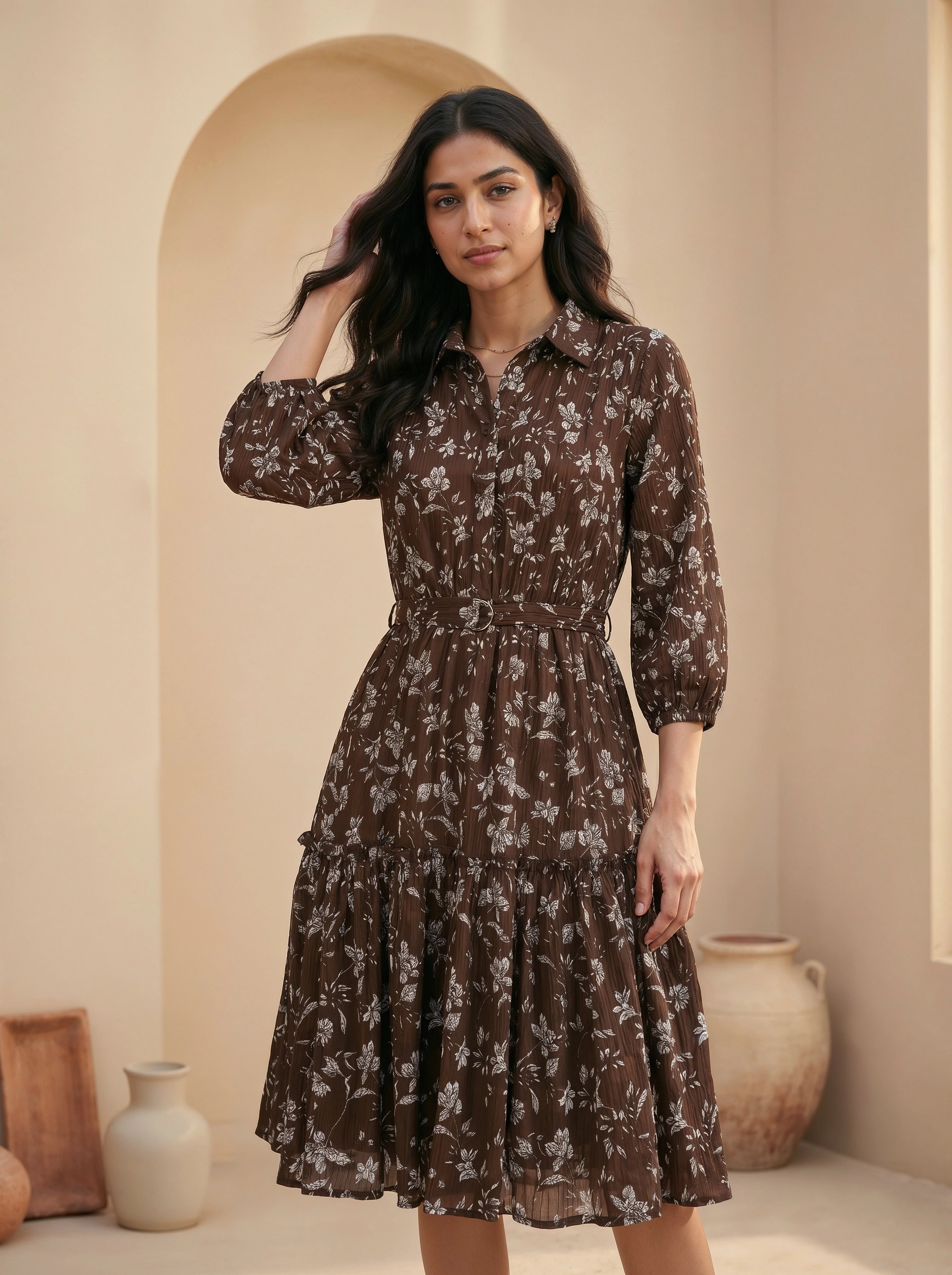 Woman wearing a brown floral dress standing in a room with beige walls and decorative vases.