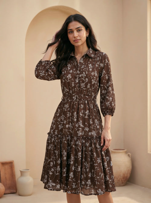 Woman wearing a brown floral dress standing in a room with beige walls and decorative vases.