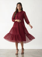 Woman wearing a burgundy dress with long sleeves and a tiered skirt on a white background