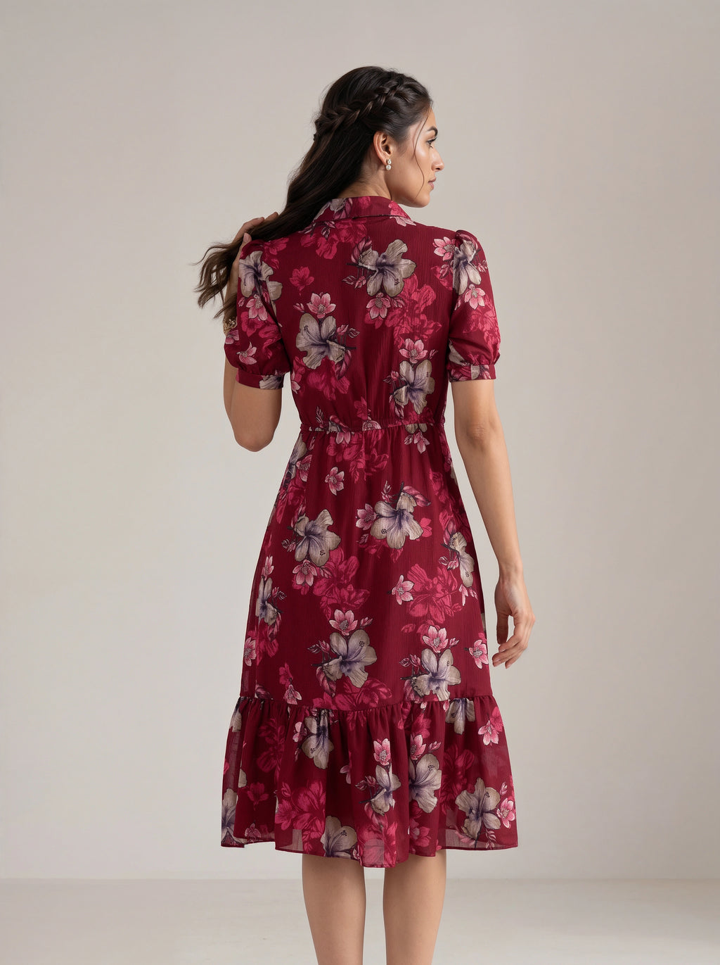 A woman wearing a short-sleeved midi dress with a floral print, shown from the back against a plain light beige studio background.