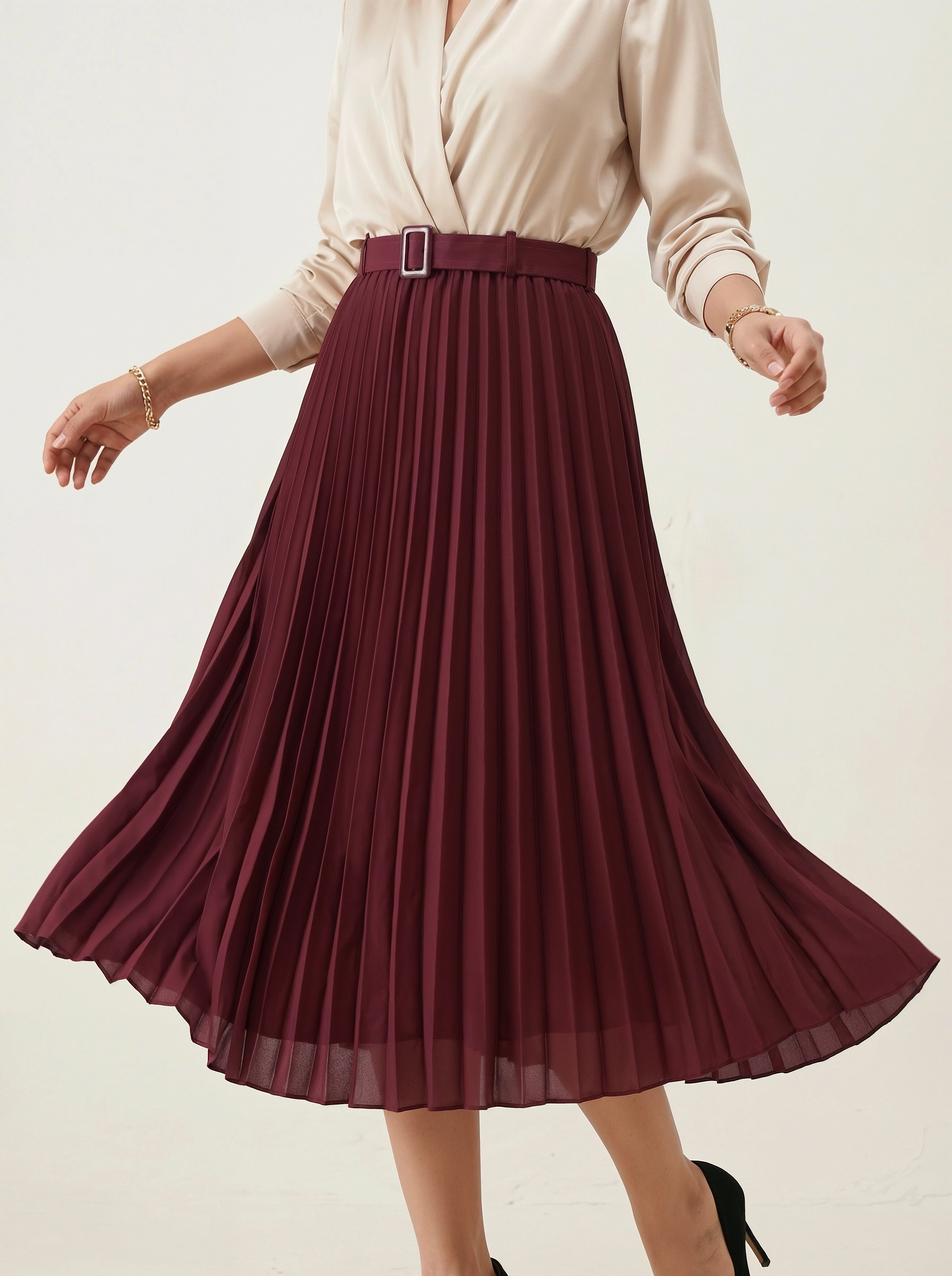 Person wearing a burgundy pleated skirt with a beige top on a light background