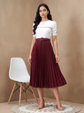 Woman wearing a white top and burgundy pleated skirt standing against a beige background.