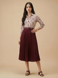 Woman wearing a patterned blouse and pleated skirt on a beige background