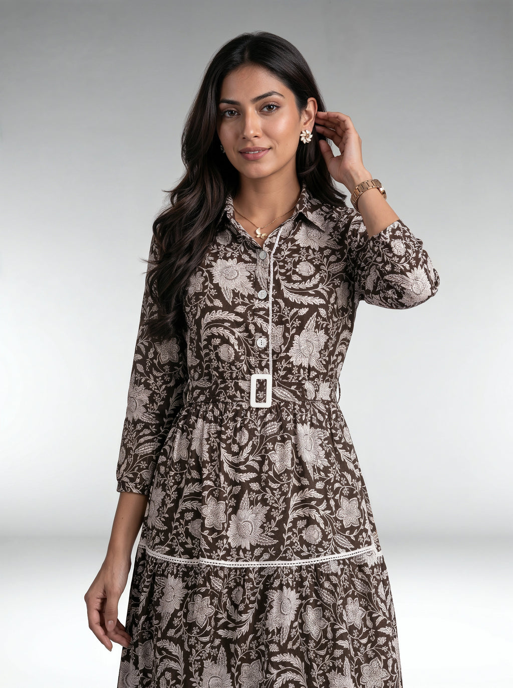 Close-up of a woman wearing a white textured long-sleeve button-front dress with a gathered waist and tiered skirt.