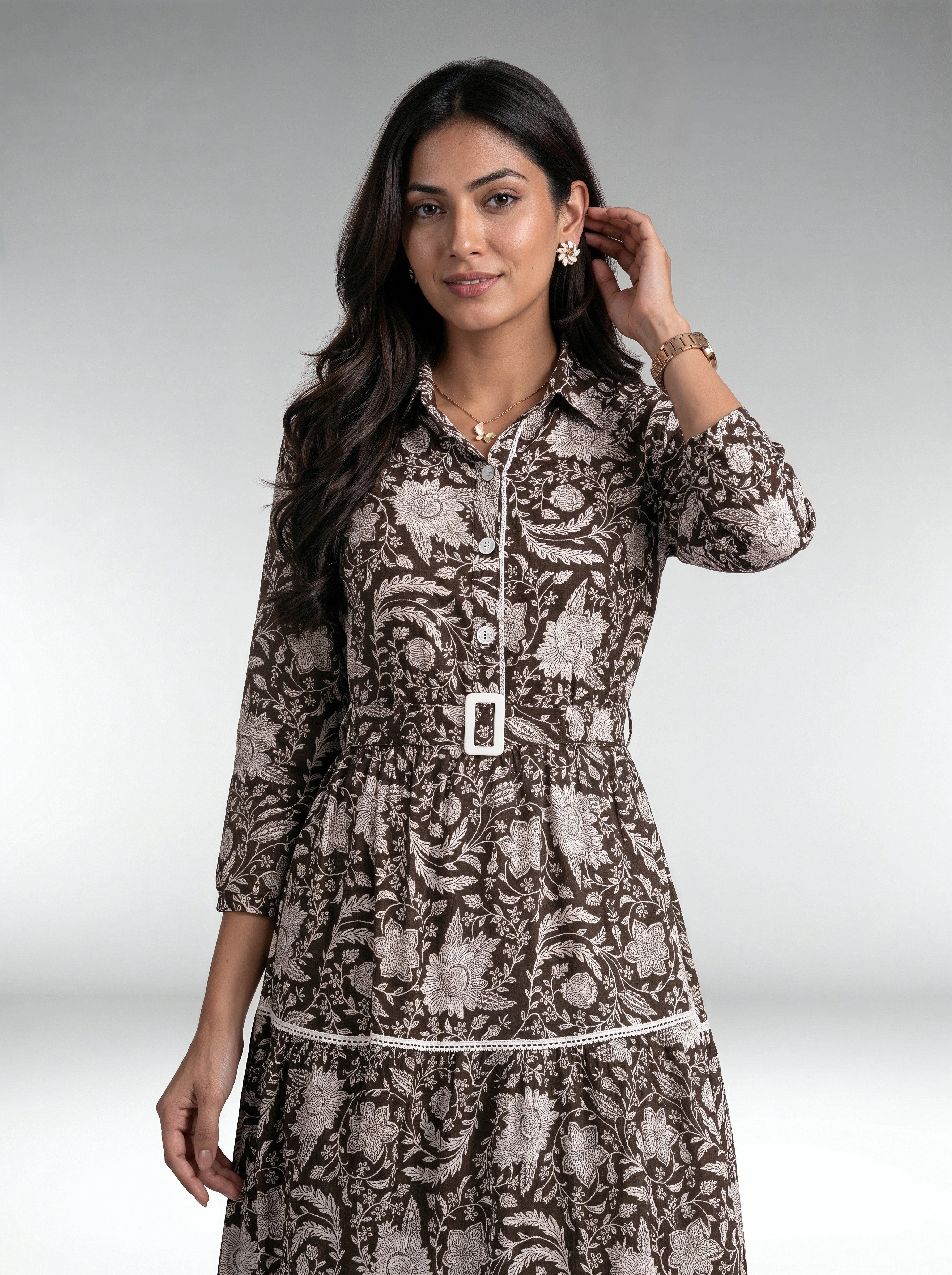 Close-up of a woman wearing a white textured long-sleeve button-front dress with a gathered waist and tiered skirt.