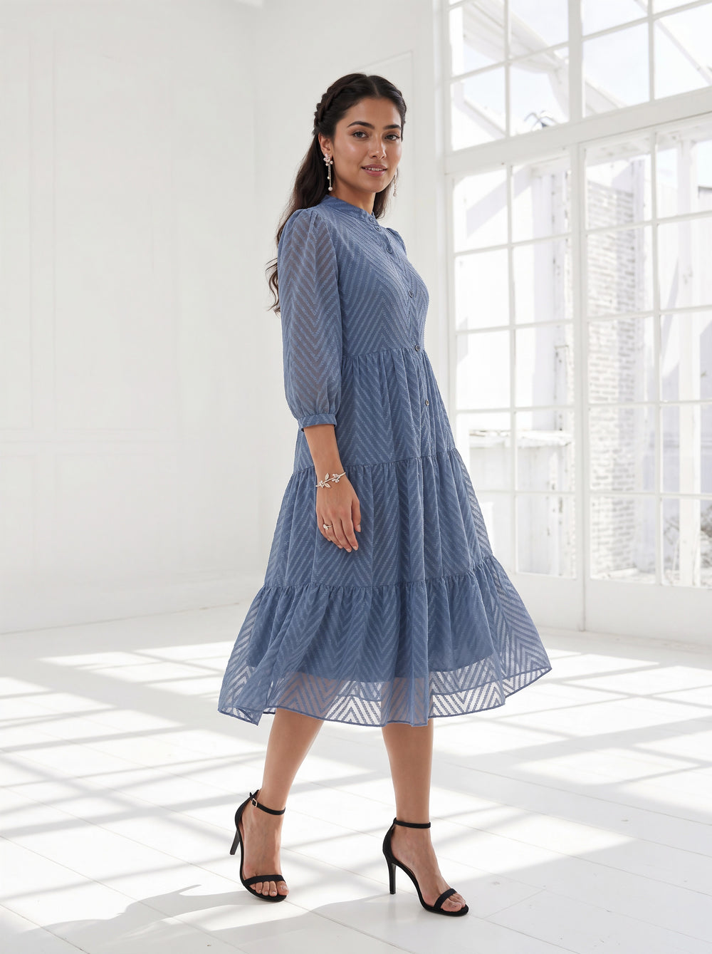 Woman wearing a blue dress standing in a bright room with large windows.
