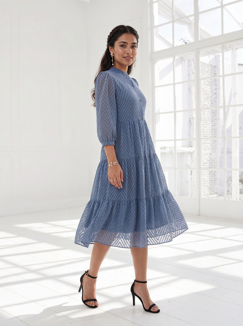 Woman wearing a blue dress standing in a bright room with large windows.