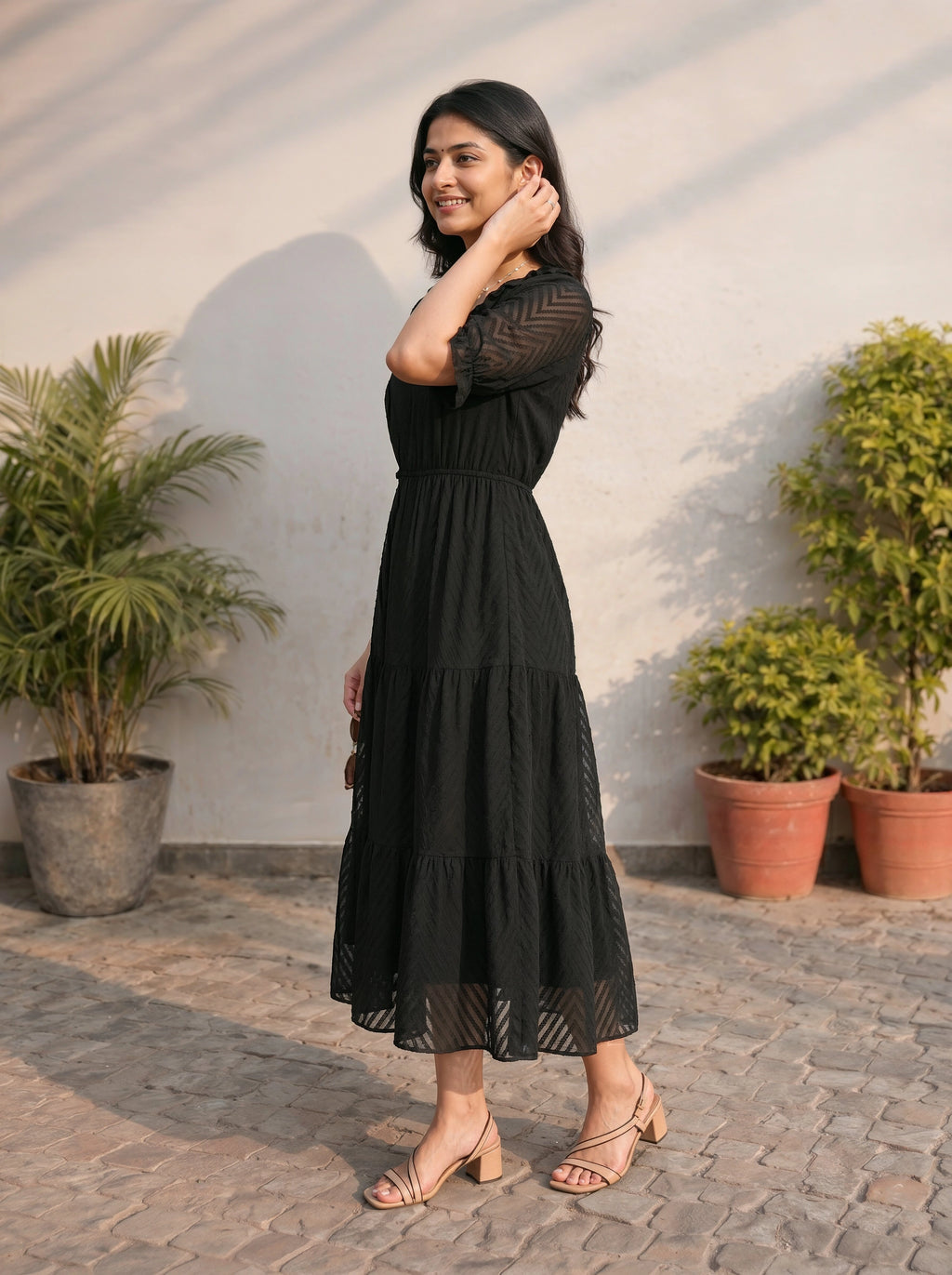 Woman in a black dress standing outdoors with plants in the background