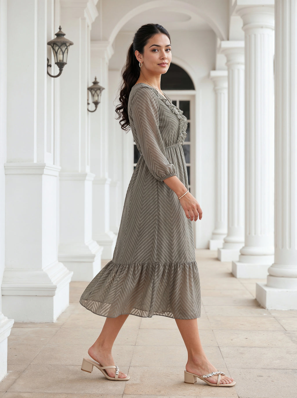 Woman in a gray dress standing in an elegant white-columned hallway.