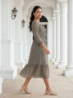 Woman in a gray dress standing in an elegant white-columned hallway.