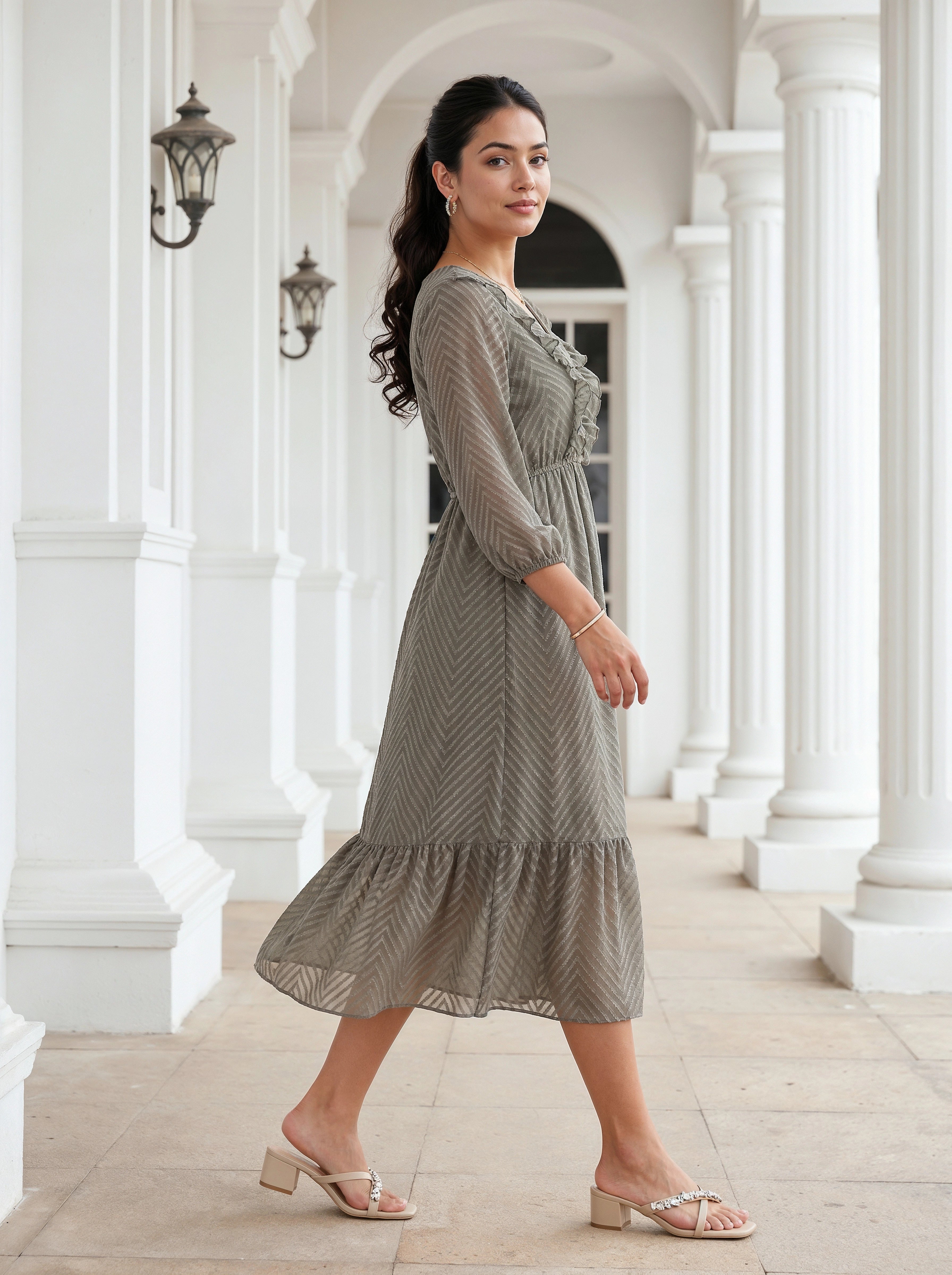 Woman in a gray dress standing in an elegant white-columned hallway.