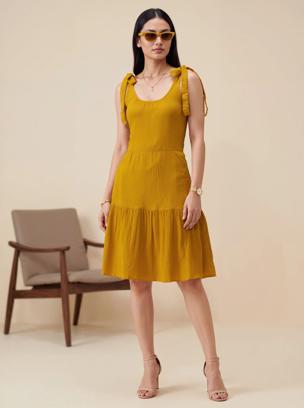 Woman wearing a mustard yellow dress with ruffled sleeves against a beige background