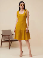 Woman wearing a mustard yellow dress with ruffled sleeves against a beige background