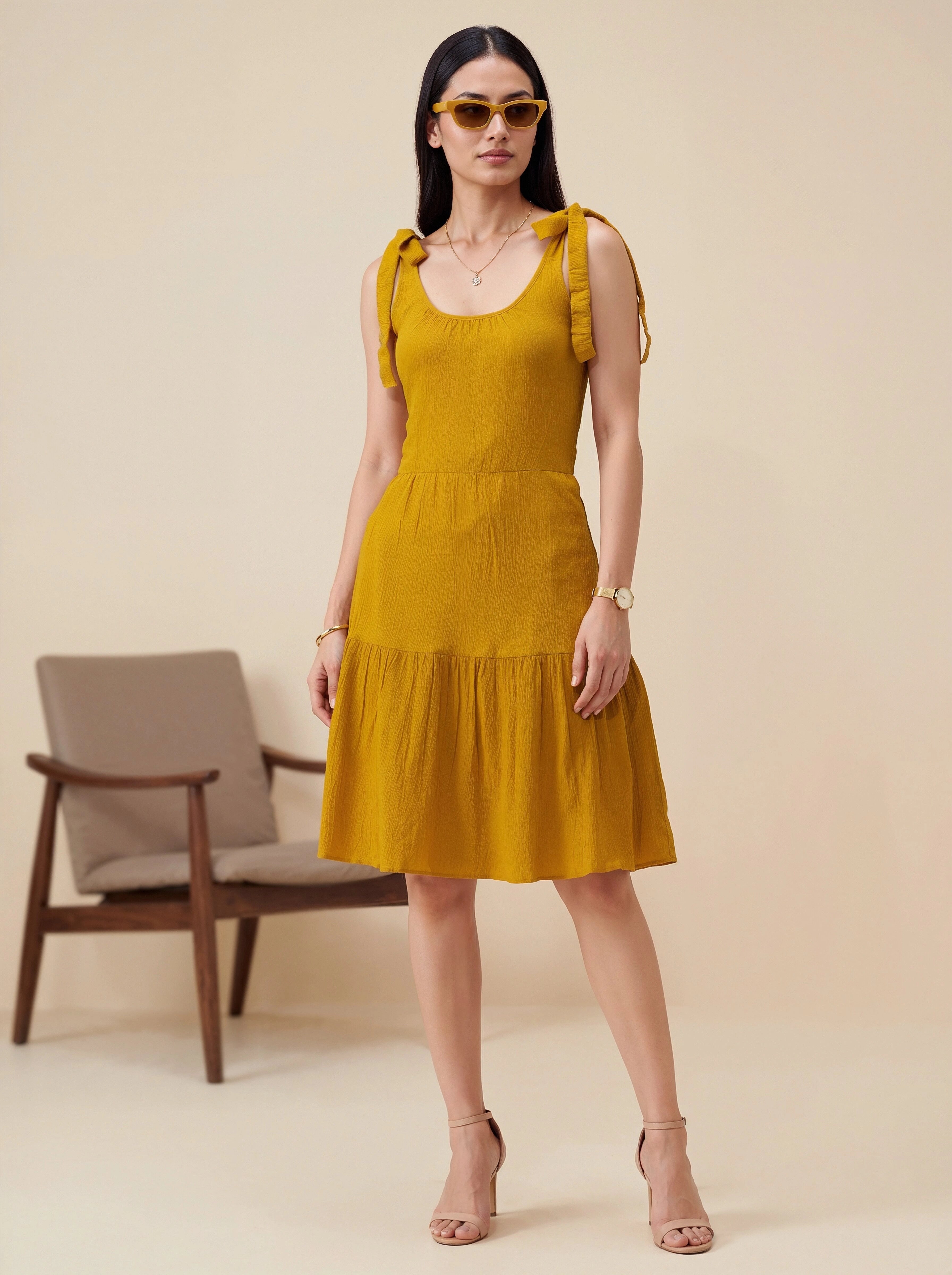 Woman wearing a mustard yellow dress with ruffled sleeves against a beige background