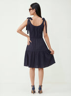 Woman wearing a navy blue dress with bow straps on a white background