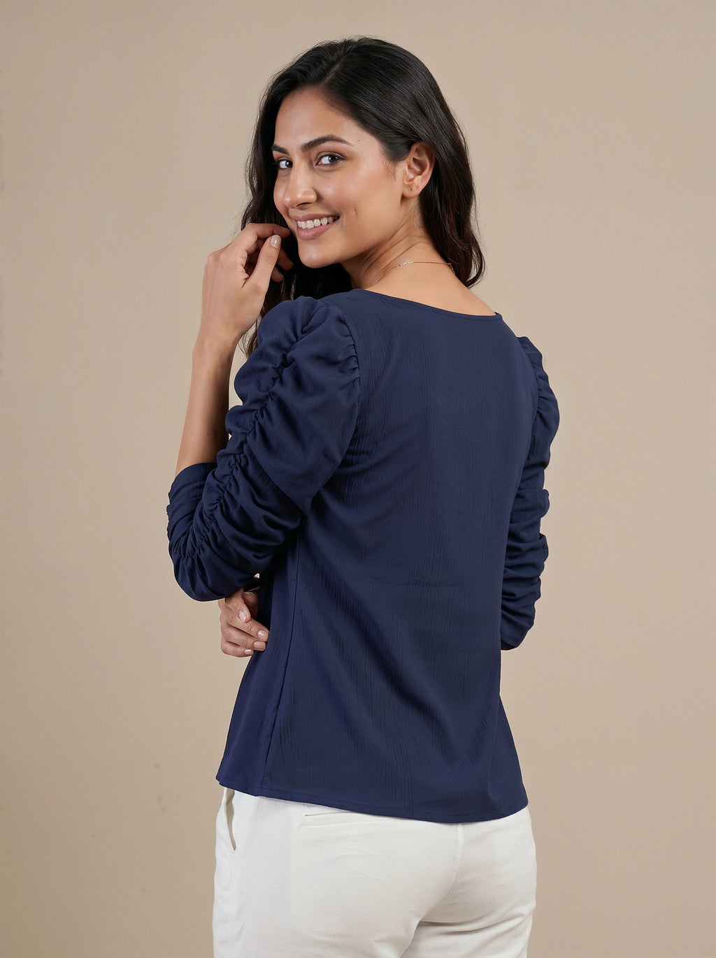 Woman wearing a navy blue blouse with ruffled sleeves on a beige background