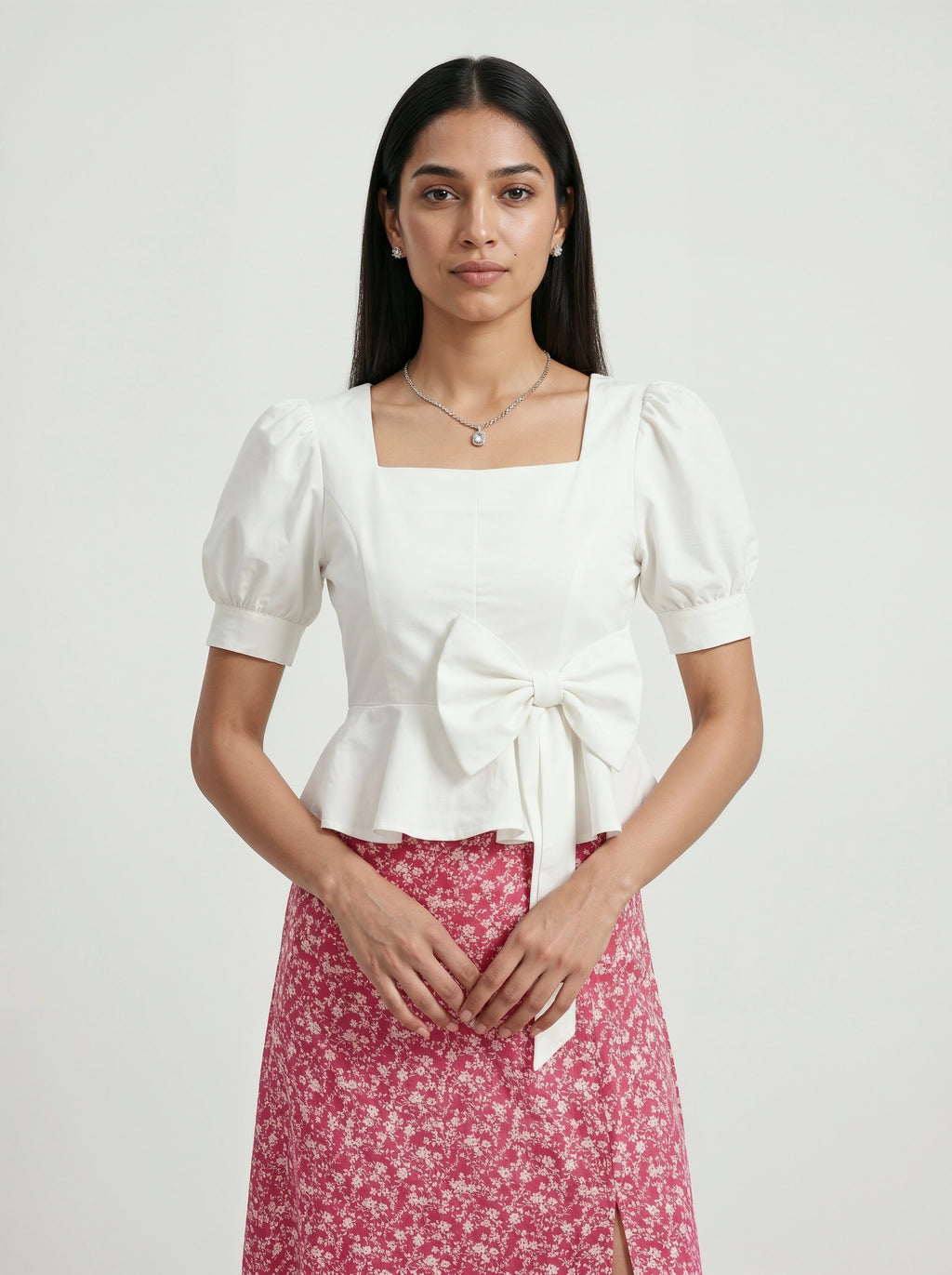 Woman wearing a white top with puff sleeves and a pink floral skirt on a light gray background