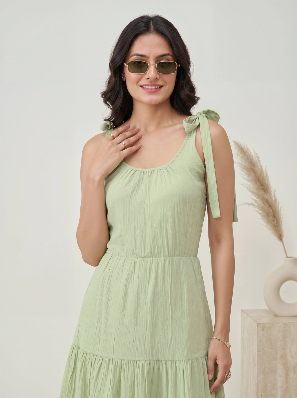 Woman wearing a light green dress with tied straps against a neutral background