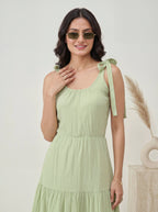 Woman wearing a light green dress with tied straps against a neutral background