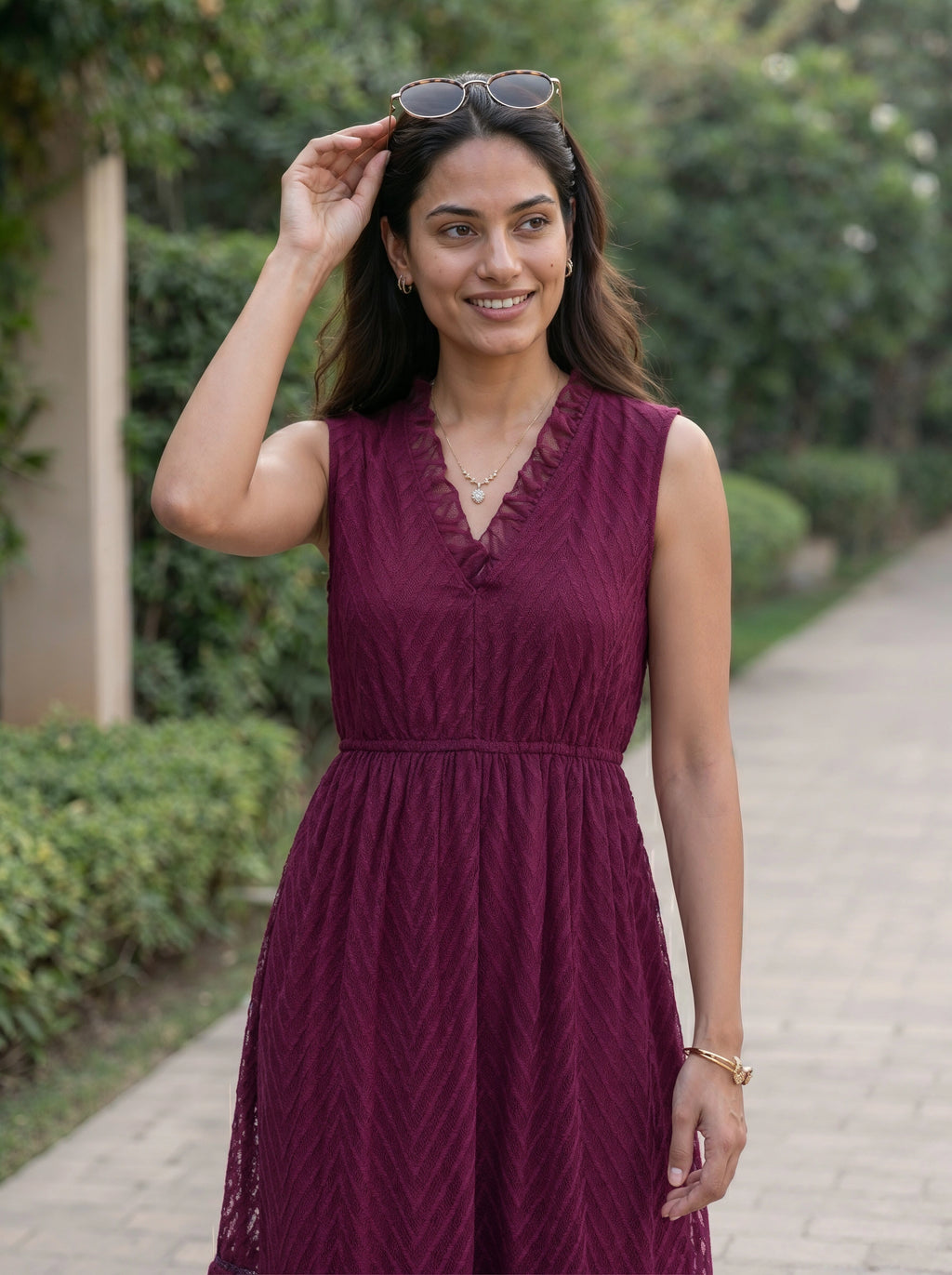 Woman in a maroon dress standing outdoors on a path with greenery.