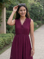 Woman in a maroon dress standing outdoors on a path with greenery.