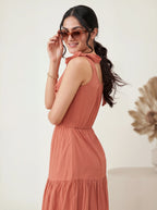Woman wearing a rust-colored dress and sunglasses, standing against a plain background.