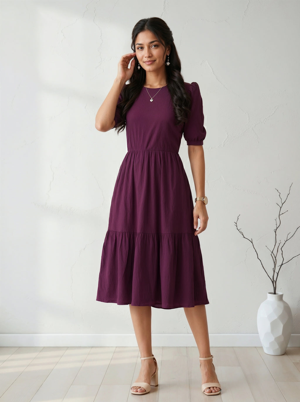 Woman wearing a purple dress standing in a room with a white wall and a vase.