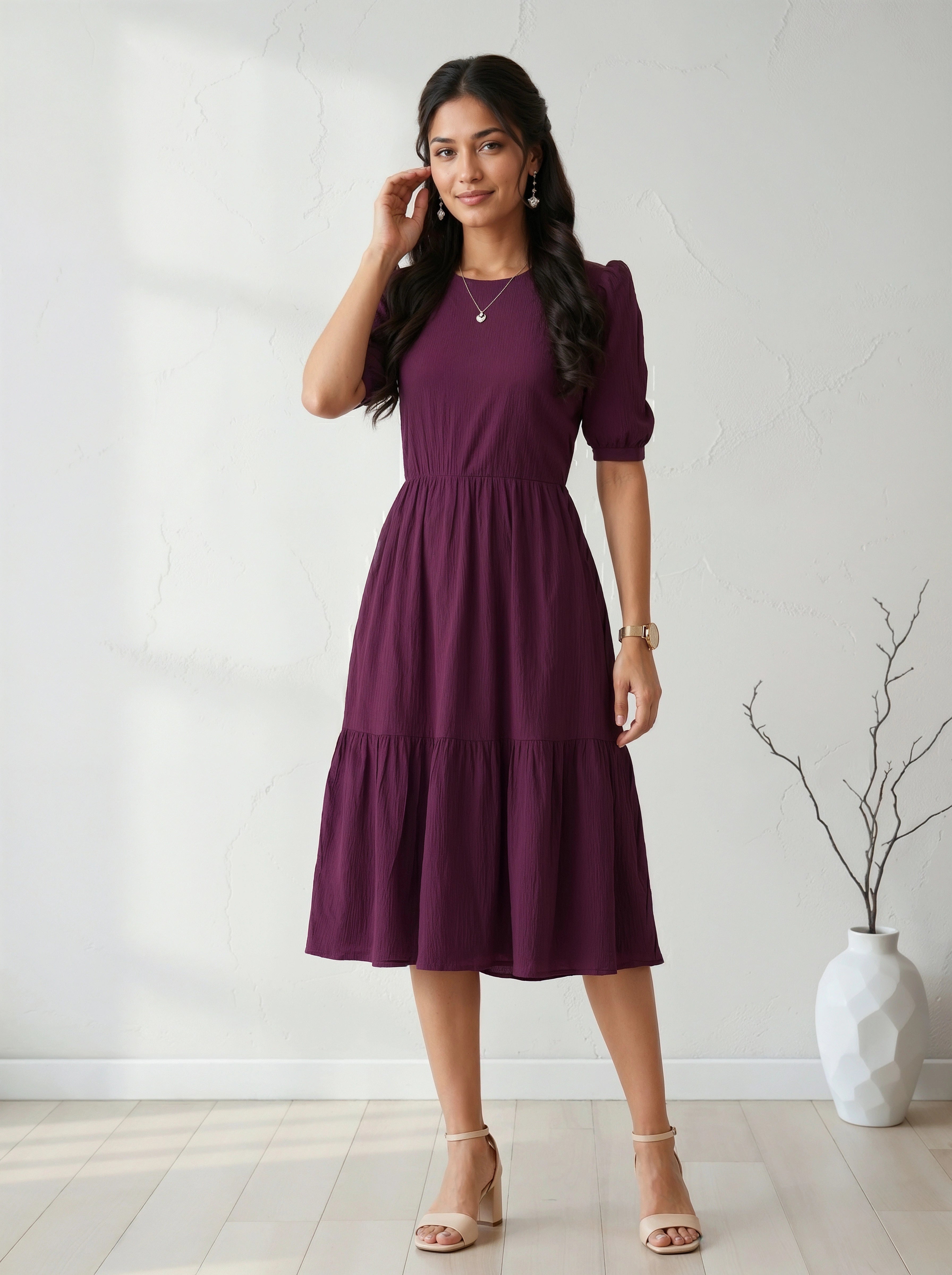 Woman wearing a purple dress standing in a room with a white wall and a vase.