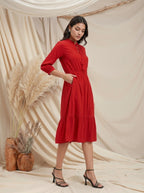 Woman in a red dress standing against a beige curtain with decorative elements.