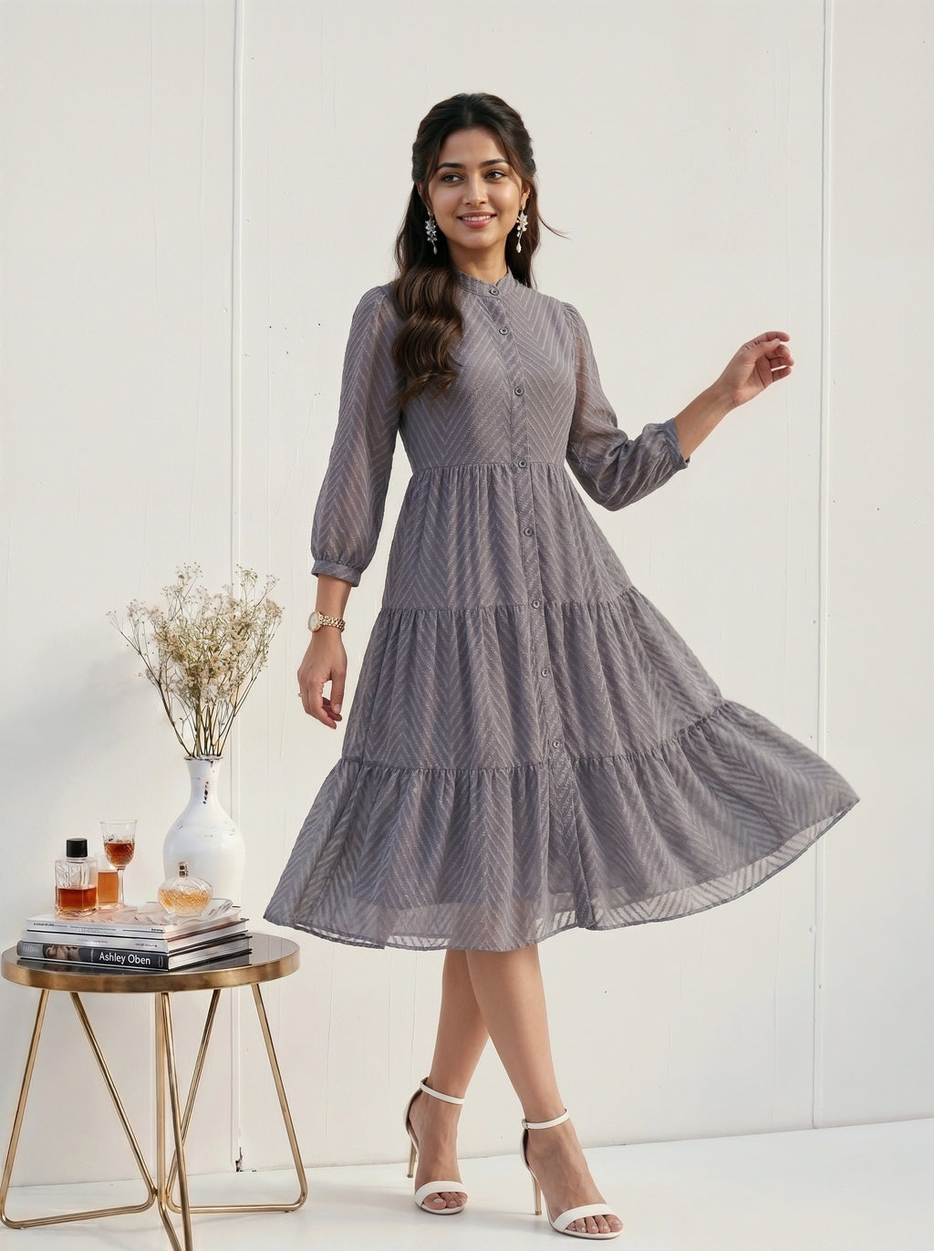 Woman in a gray patterned dress standing next to a small table with decor items on a white background