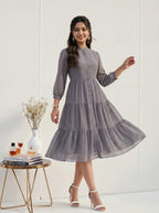 Woman in a gray patterned dress standing next to a small table with decor items on a white background